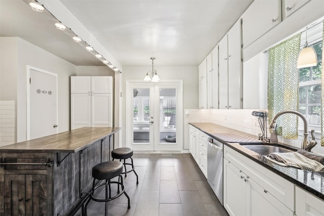 3923 Maquoketa Dr, Des Moines, IA 50311 - kitchen featuring stainless steel dishwasher, white cabinetry, tasteful backsplash, dark tile patterned floors, and a breakfast bar
