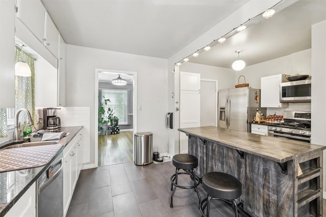 3923 Maquoketa Dr, Des Moines, IA 50311 - kitchen featuring appliances with stainless steel finishes, tasteful backsplash, white cabinetry, a kitchen bar, and wooden counters