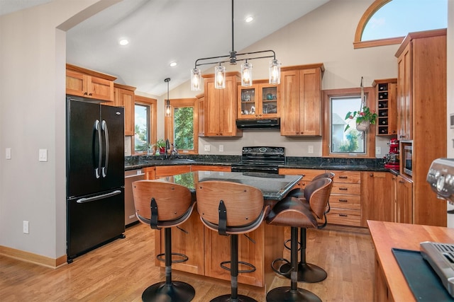 13001 Twana Dr, Urbandale, IA 50323 - kitchen featuring black appliances, under cabinet range hood, vaulted ceiling, light wood-style flooring, and a breakfast bar