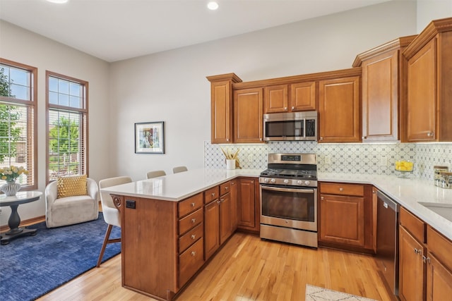 3607 152nd St, Urbandale, IA 50323 - kitchen with appliances with stainless steel finishes, a peninsula, light wood finished floors, a breakfast bar, and brown cabinets