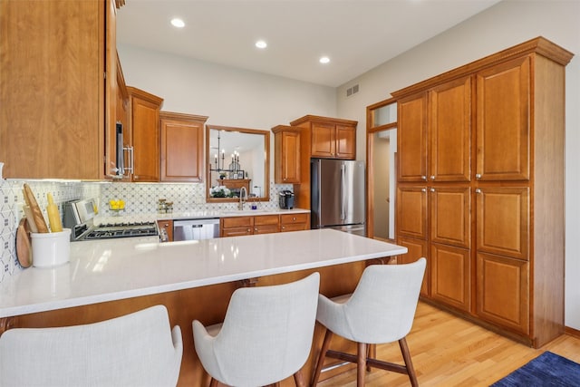 3607 152nd St, Urbandale, IA 50323 - kitchen featuring stainless steel appliances, a peninsula, light countertops, backsplash, and light wood-style floors