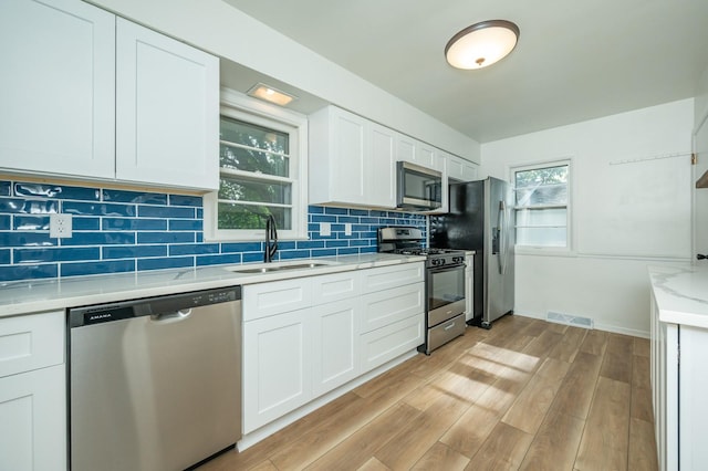 1205 Elder Ln, Des Moines, IA 50315 - kitchen with stainless steel appliances, tasteful backsplash, white cabinetry, light wood finished floors, and light stone countertops