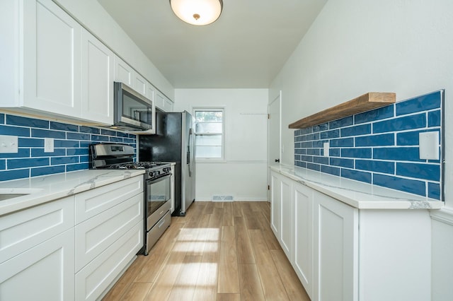 1205 Elder Ln, Des Moines, IA 50315 - kitchen with appliances with stainless steel finishes, tasteful backsplash, white cabinets, light wood-style floors, and light stone countertops