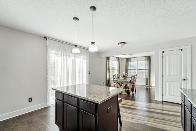 3504 Hawthorn Dr SW, Bondurant, IA 50035 - kitchen featuring dark wood-style flooring, pendant lighting, light stone countertops, a kitchen bar, and a textured ceiling
