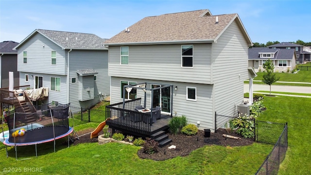 1208 NE 21st St, Grimes, IA 50111 - back of house with a wooden deck, a trampoline, a fenced backyard, a shingled roof, and stairway