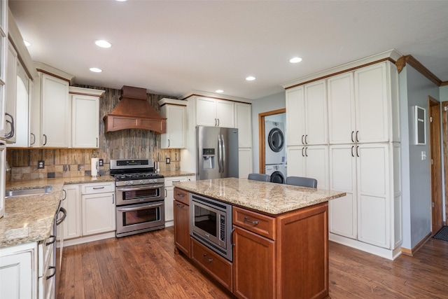 4785 Windsor Cir, Pleasant Hill, IA 50327 - kitchen with appliances with stainless steel finishes, stacked washing machine and dryer, premium range hood, tasteful backsplash, and dark wood-style floors
