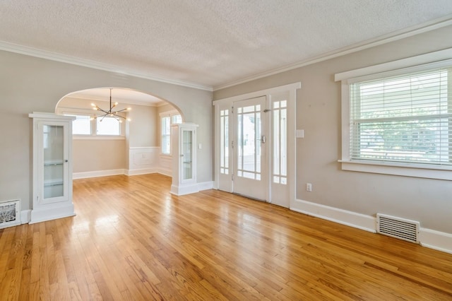 849 39th St, Des Moines, IA 50312 - unfurnished room featuring a textured ceiling, arched walkways, a chandelier, light wood-style flooring, and crown molding