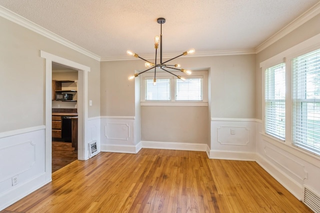 849 39th St, Des Moines, IA 50312 - unfurnished dining area featuring a chandelier, wainscoting, light wood-type flooring, a textured ceiling, and crown molding