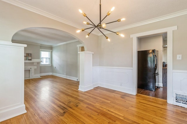 849 39th St, Des Moines, IA 50312 - unfurnished room with arched walkways, crown molding, light wood-style floors, a chandelier, and a wainscoted wall