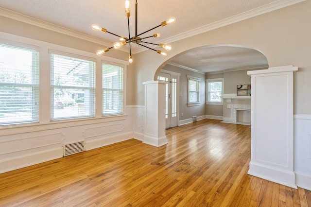 849 39th St, Des Moines, IA 50312 - unfurnished living room with arched walkways, light wood-style flooring, wainscoting, ornamental molding, and a chandelier