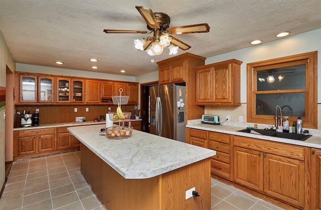 1612 Horse N Buggy Dr, Adel, IA 50003 - kitchen featuring stainless steel refrigerator with ice dispenser, brown cabinets, a kitchen island, light tile patterned floors, and a textured ceiling