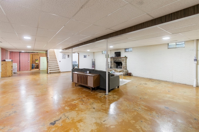 122 G76 Hwy, Lacona, IA 50139 - living area featuring a drop ceiling, a stone fireplace, finished concrete flooring, stairs, and brick wall