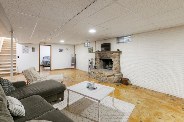 122 G76 Hwy, Lacona, IA 50139 - living room with a stone fireplace, concrete flooring, a paneled ceiling, stairway, and brick wall