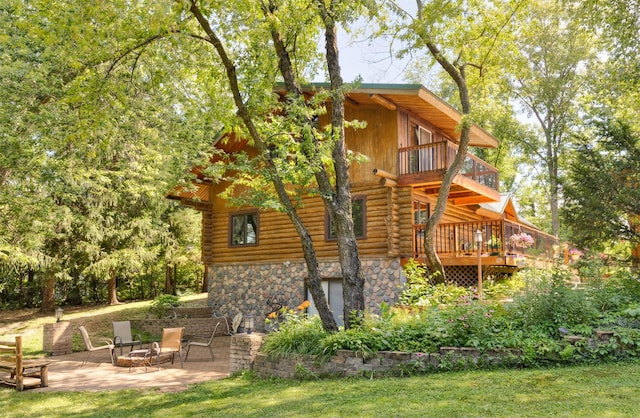 702 Jasper Ave NE, Mitchellville, IA 50169 - rear view of house with log siding, a patio area, stone siding, a deck, and an outdoor fire pit