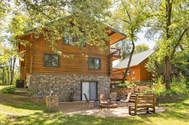 702 Jasper Ave NE, Mitchellville, IA 50169 - rear view of house featuring log exterior, stone siding, a patio, a deck, and a lawn