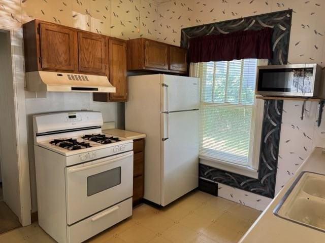4046 4th St, Des Moines, IA 50313 - kitchen with white appliances, under cabinet range hood, light flooring, plenty of natural light, and wallpapered walls