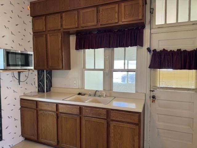 4046 4th St, Des Moines, IA 50313 - kitchen with stainless steel microwave, wallpapered walls, brown cabinets, and light countertops
