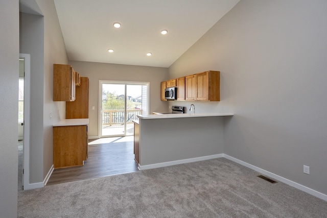 1102 Westview Dr, Huxley, IA 50124 - kitchen featuring stainless steel microwave, range, carpet, vaulted ceiling, and a peninsula