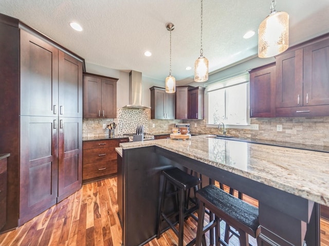 36508 Meadow Ln, Cumming, IA 50061 - kitchen featuring wall chimney exhaust hood, a breakfast bar area, decorative backsplash, light wood-style floors, and hanging light fixtures