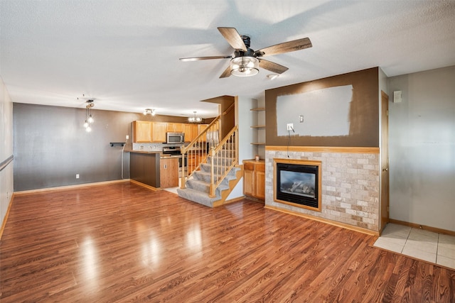 1517 SE Delaware Ave Unit 2, Ankeny, IA 50021 - unfurnished living room featuring a ceiling fan, stairway, wood finished floors, a glass covered fireplace, and a textured ceiling