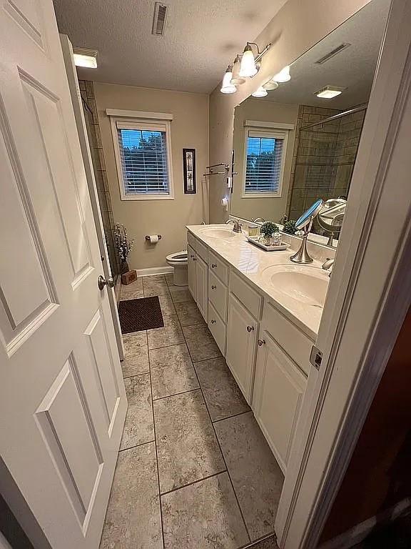 2279 Pheasant Ridge Ln, Ames, IA 50010 - bathroom with double vanity, tiled shower, a textured ceiling, and tile patterned flooring