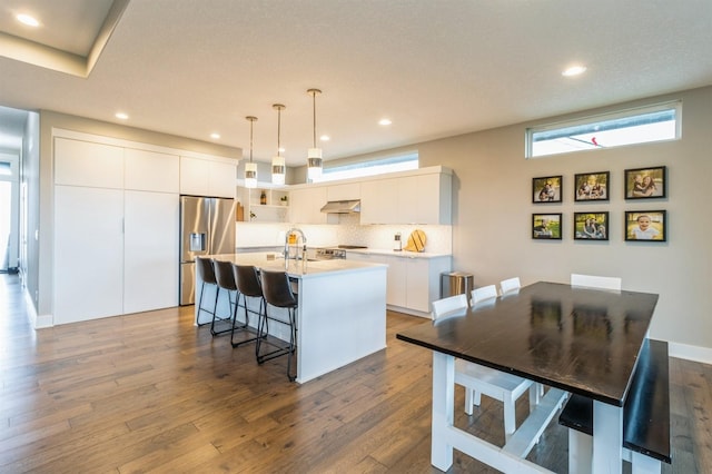 905 NE Badger Ln, Waukee, IA 50263 - kitchen featuring stainless steel refrigerator with ice dispenser, under cabinet range hood, a kitchen breakfast bar, backsplash, and dark wood-style floors