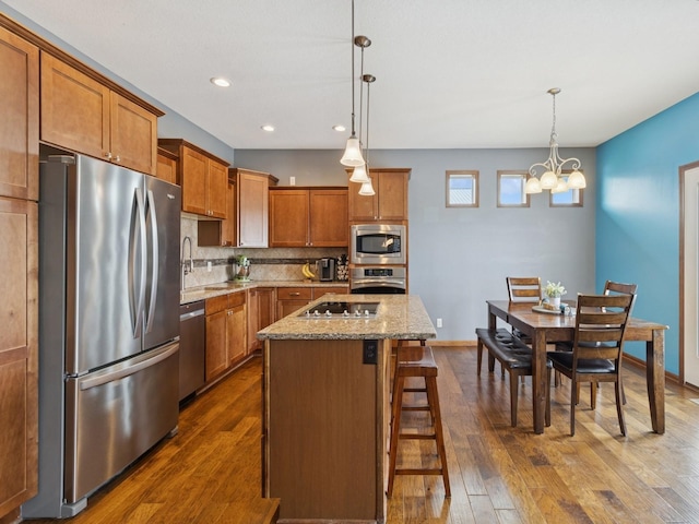 2458 SE 108th St, Runnells, IA 50237 - kitchen with stainless steel appliances, brown cabinetry, a chandelier, dark wood-type flooring, and tasteful backsplash