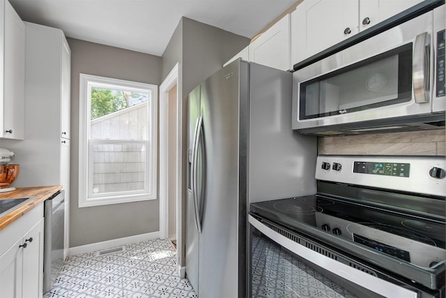 3315 61st St, Des Moines, IA 50322 - kitchen with appliances with stainless steel finishes, white cabinetry, wood counters, backsplash, and light tile patterned floors
