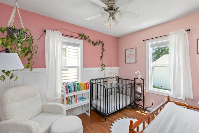 3315 61st St, Des Moines, IA 50322 - bedroom featuring wood finished floors, wainscoting, a crib, and ceiling fan