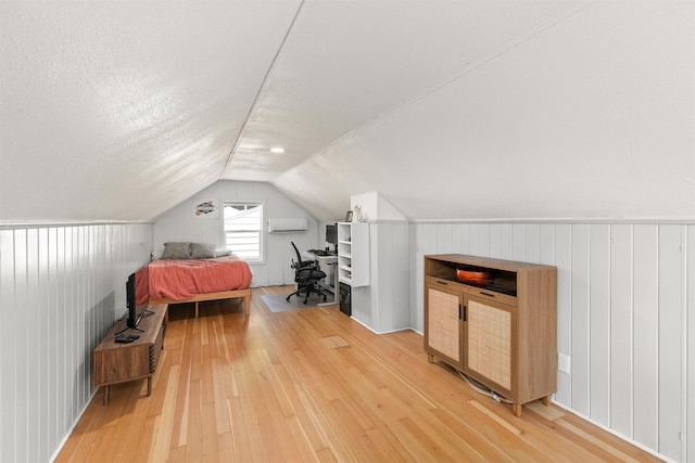 3315 61st St, Des Moines, IA 50322 - bedroom with light wood finished floors, vaulted ceiling, an AC wall unit, and a textured ceiling