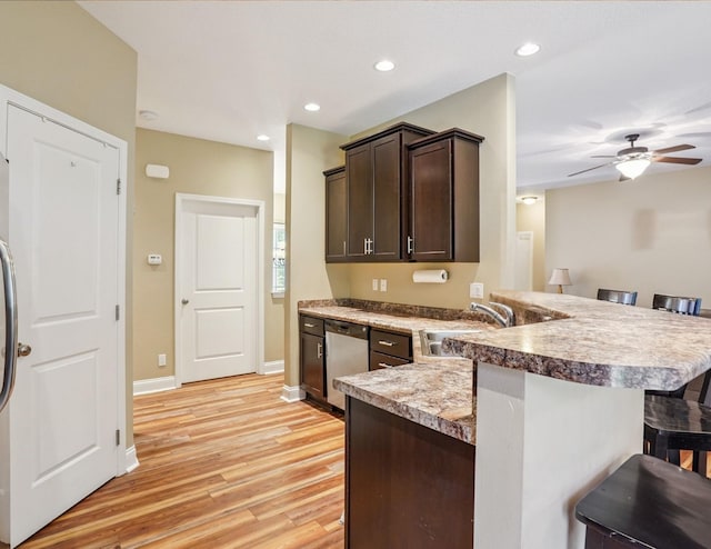 929 Sampson Dr, Nevada, IA 50201 - kitchen with stainless steel dishwasher, a kitchen bar, dark brown cabinetry, light wood-type flooring, and a peninsula