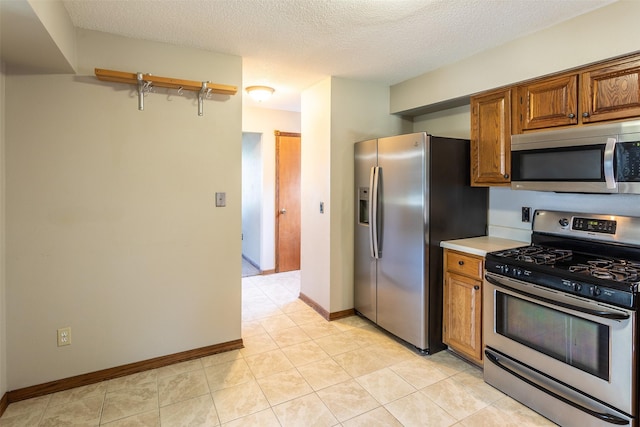 4624 Tamara Ln, West Des Moines, IA 50265 - kitchen with appliances with stainless steel finishes, brown cabinetry, light countertops, a textured ceiling, and light tile patterned flooring