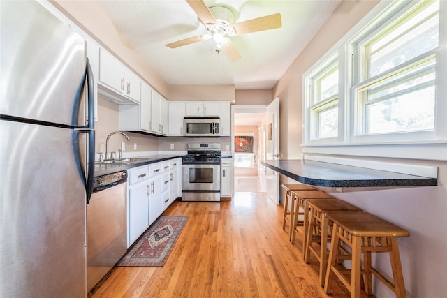 2521 40th St, Des Moines, IA 50310 - kitchen with stainless steel appliances, light wood finished floors, white cabinetry, a ceiling fan, and dark countertops