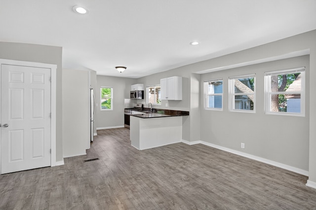 1728 NW Dr, Des Moines, IA 50310 - kitchen with appliances with stainless steel finishes, wood finished floors, a peninsula, open floor plan, and white cabinets
