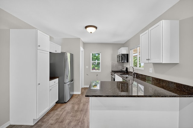 1728 NW Dr, Des Moines, IA 50310 - kitchen with appliances with stainless steel finishes, dark stone counters, light wood finished floors, a peninsula, and white cabinetry
