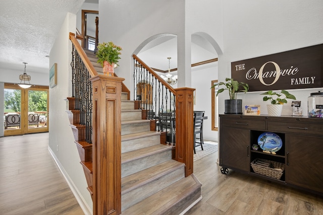 4309 129th St, Urbandale, IA 50323 - staircase with wood finished floors, a chandelier, arched walkways, a textured ceiling, and a high ceiling