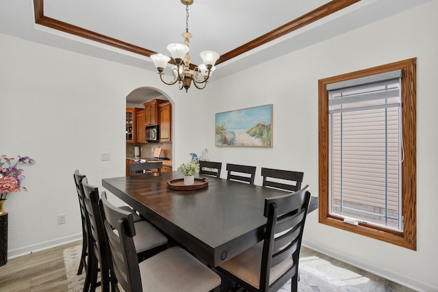 4309 129th St, Urbandale, IA 50323 - dining area with arched walkways, a raised ceiling, a chandelier, light wood-style floors, and ornamental molding
