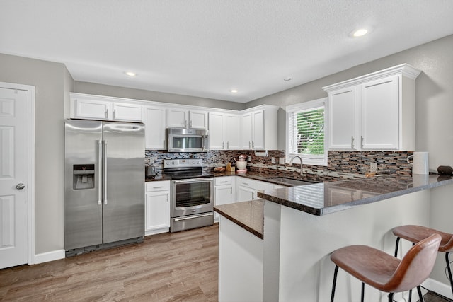 4808 Dewey Pl, Johnston, IA 50131 - kitchen with stainless steel appliances, white cabinets, a peninsula, decorative backsplash, and a breakfast bar