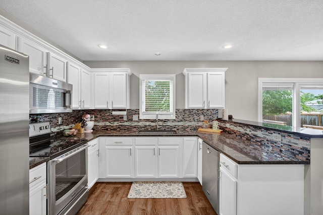 4808 Dewey Pl, Johnston, IA 50131 - kitchen featuring stainless steel appliances, a peninsula, wood finished floors, decorative backsplash, and white cabinetry