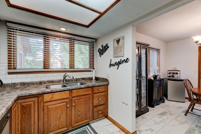 1116 42nd St, West Des Moines, IA 50266 - kitchen featuring light marble finish floors, brown cabinets, a textured ceiling, and plenty of natural light