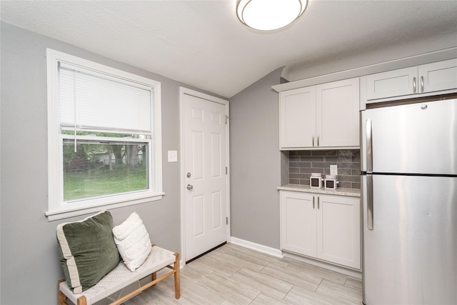 2512 Boston Ave, Des Moines, IA 50310 - kitchen featuring freestanding refrigerator, tasteful backsplash, vaulted ceiling, white cabinetry, and light stone counters