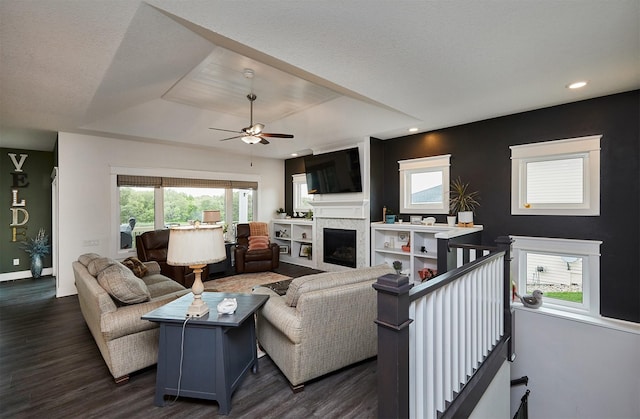 685 Indian Ridge Dr, Waukee, IA 50263 - living area featuring a raised ceiling, dark wood-style floors, ceiling fan, a fireplace, and healthy amount of natural light