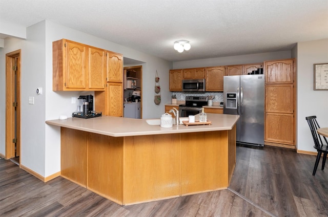 14449 Briarwood Ln, Urbandale, IA 50323 - kitchen featuring appliances with stainless steel finishes, a peninsula, light countertops, dark wood-style flooring, and separate washer and dryer