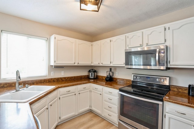 681 63rd St, West Des Moines, IA 50266 - kitchen featuring appliances with stainless steel finishes, white cabinets, dark countertops, and light wood-type flooring