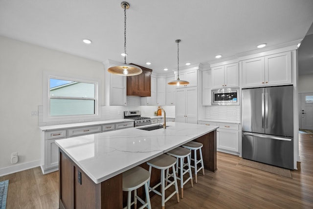 2309 NW 29th St, Ankeny, IA 50023 - kitchen featuring stainless steel appliances, decorative backsplash, white cabinets, wood finished floors, and a kitchen island with sink