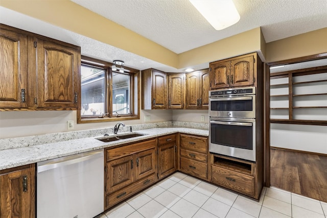 6542 Washington Ave, Windsor Heights, IA 50324 - kitchen featuring stainless steel appliances, a textured ceiling, light stone counters, light tile patterned floors, and brown cabinets