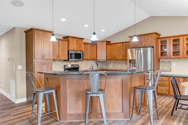 2501 NE Ewing Ct, Grimes, IA 50111 - kitchen with appliances with stainless steel finishes, light wood finished floors, a kitchen bar, brown cabinets, and vaulted ceiling
