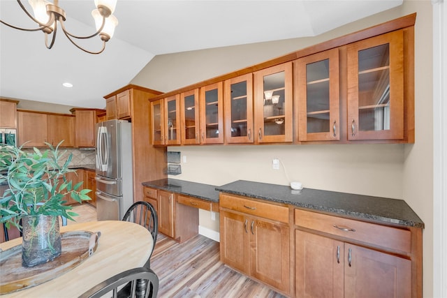 2501 NE Ewing Ct, Grimes, IA 50111 - kitchen featuring stainless steel appliances, brown cabinetry, vaulted ceiling, decorative backsplash, and light wood finished floors