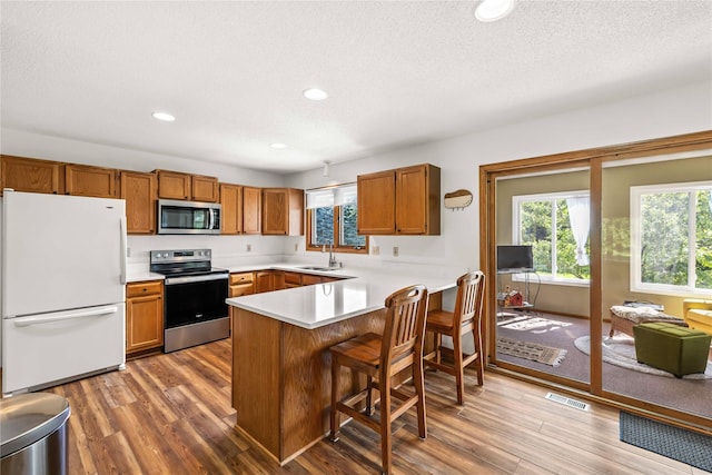 9421 NE 28th Ct, Ankeny, IA 50021 - kitchen featuring appliances with stainless steel finishes, wood finished floors, a peninsula, light countertops, and brown cabinets