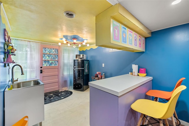 1416 Clinton Ave, Des Moines, IA 50313 - kitchen featuring a peninsula, light marble finish flooring, a breakfast bar, and a chandelier
